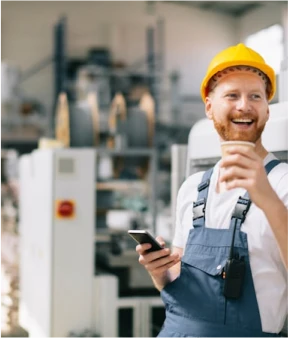 Medewerker in de industrie met helm en smartphone in een moderne productielocatie.