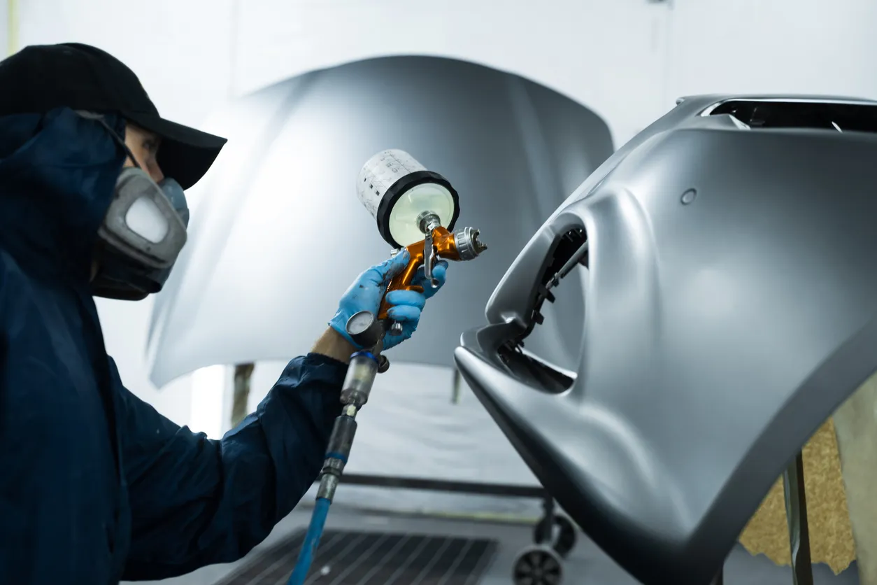 Autospuiter brengt lak aan op een auto-onderdeel in een spuitcabine.