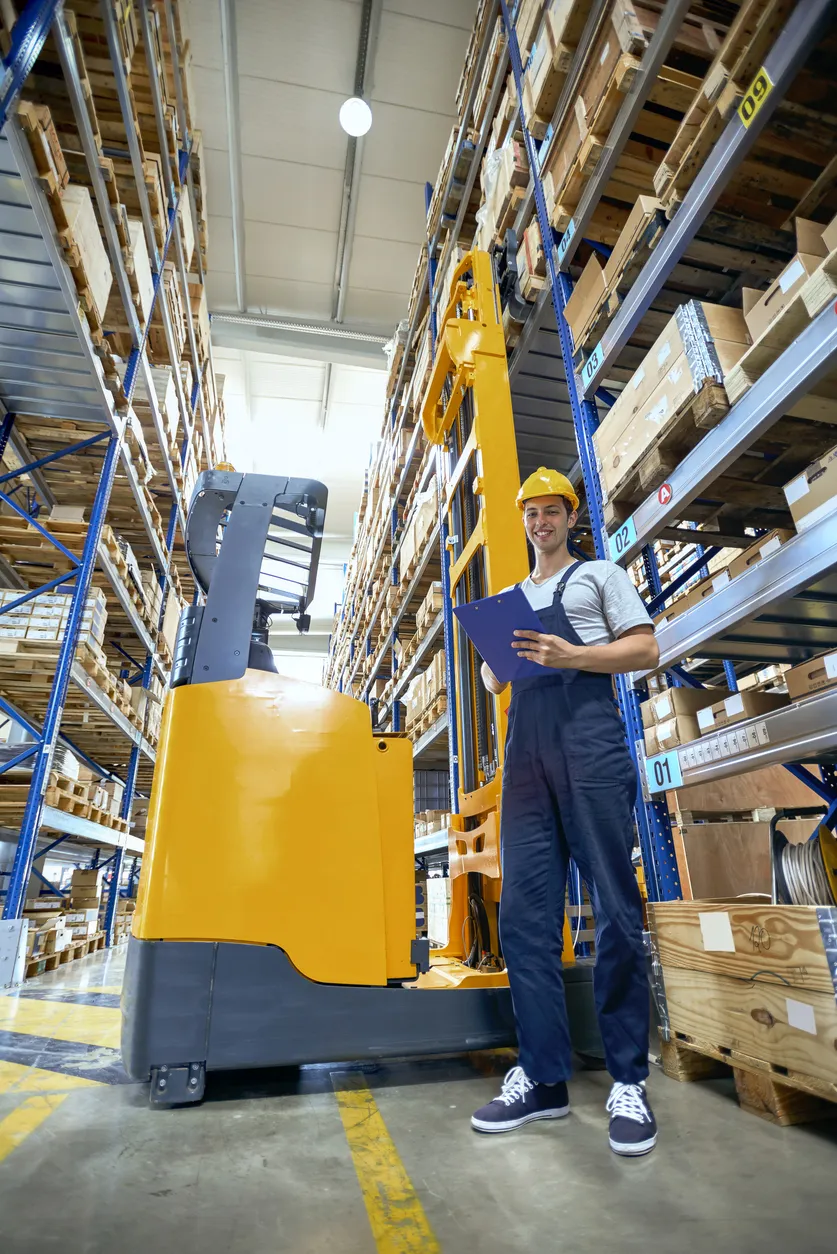 Magazijnmedewerker met heftruck en clipboard in een groot magazijn.