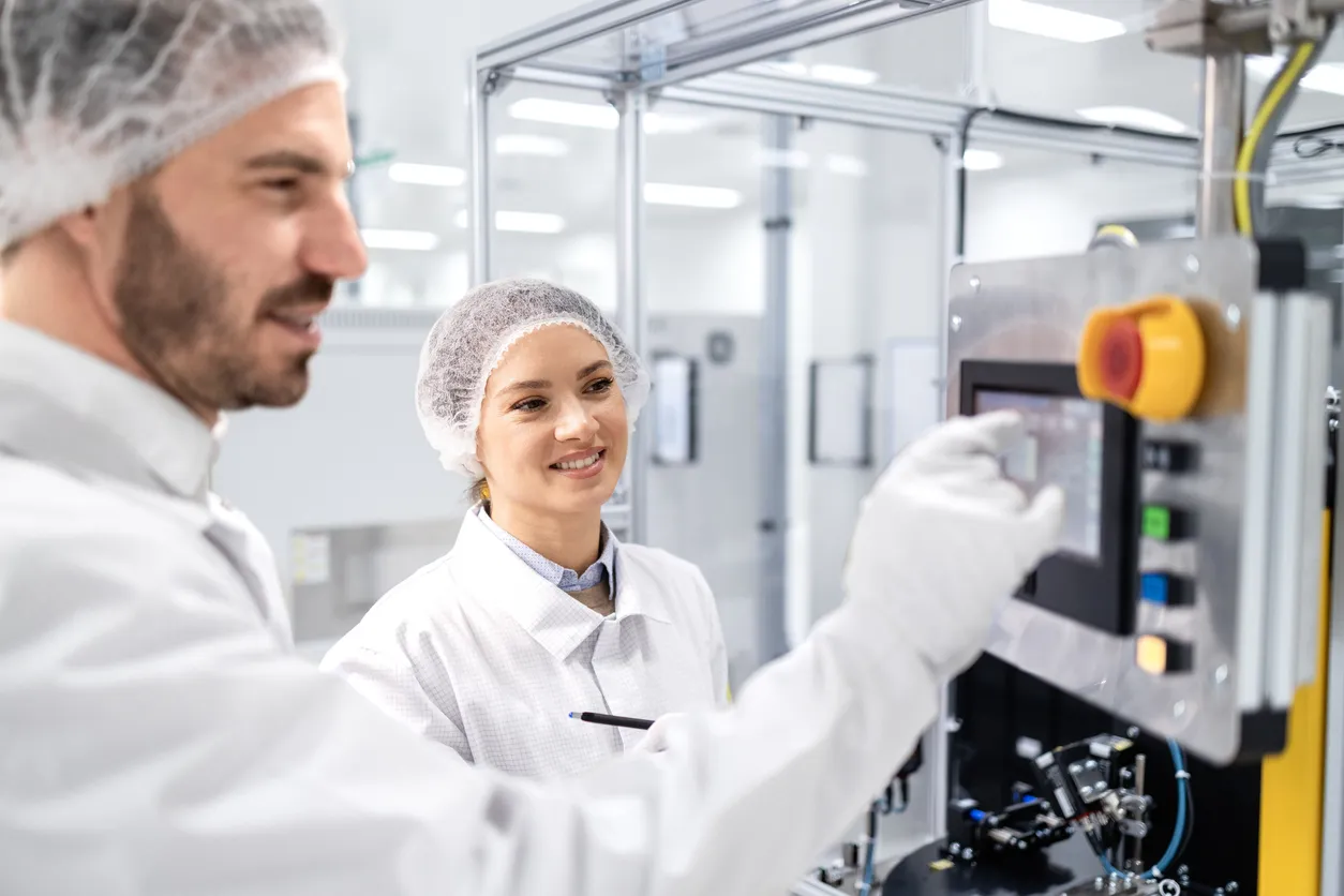 Medewerkers in een productieruimte bedienen een machinepaneel met beschermende kleding.