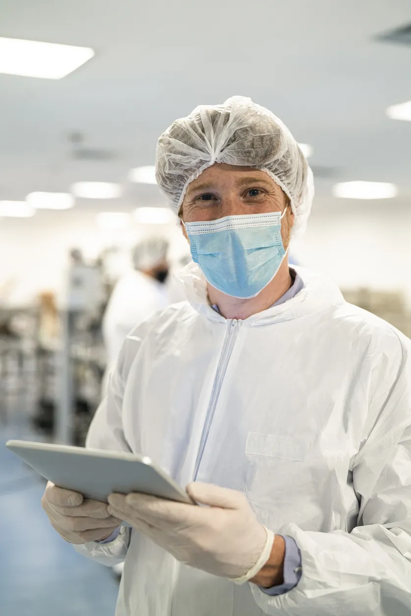 Medewerker in beschermende kleding met tablet in cleanroomomgeving voor productie of logistiek werk in Nederland.