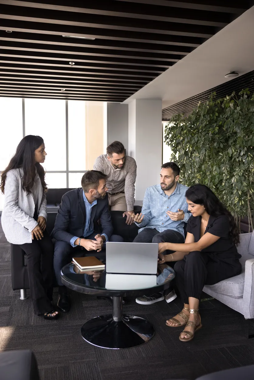 Team medewerkers in overleg aan een tafel met laptop in een moderne kantooromgeving.