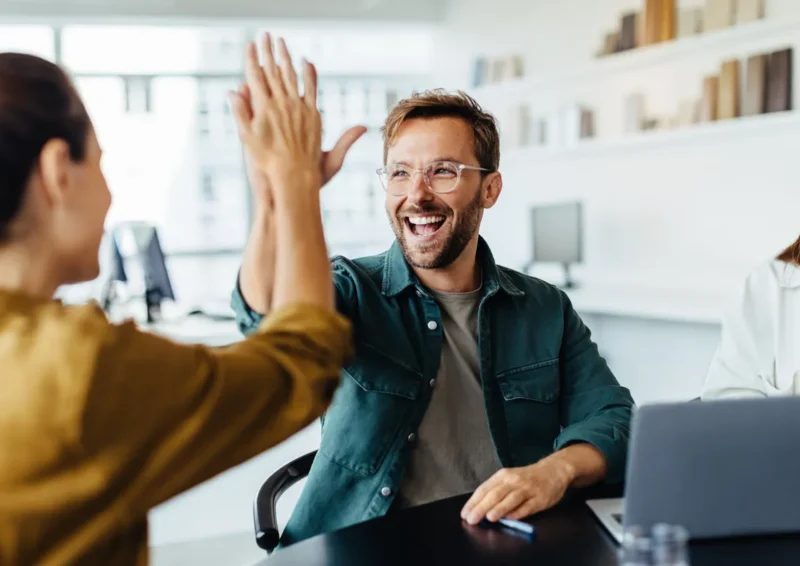 Teamleden in een kantoor die elkaar een high five geven bij een succesvolle samenwerking.